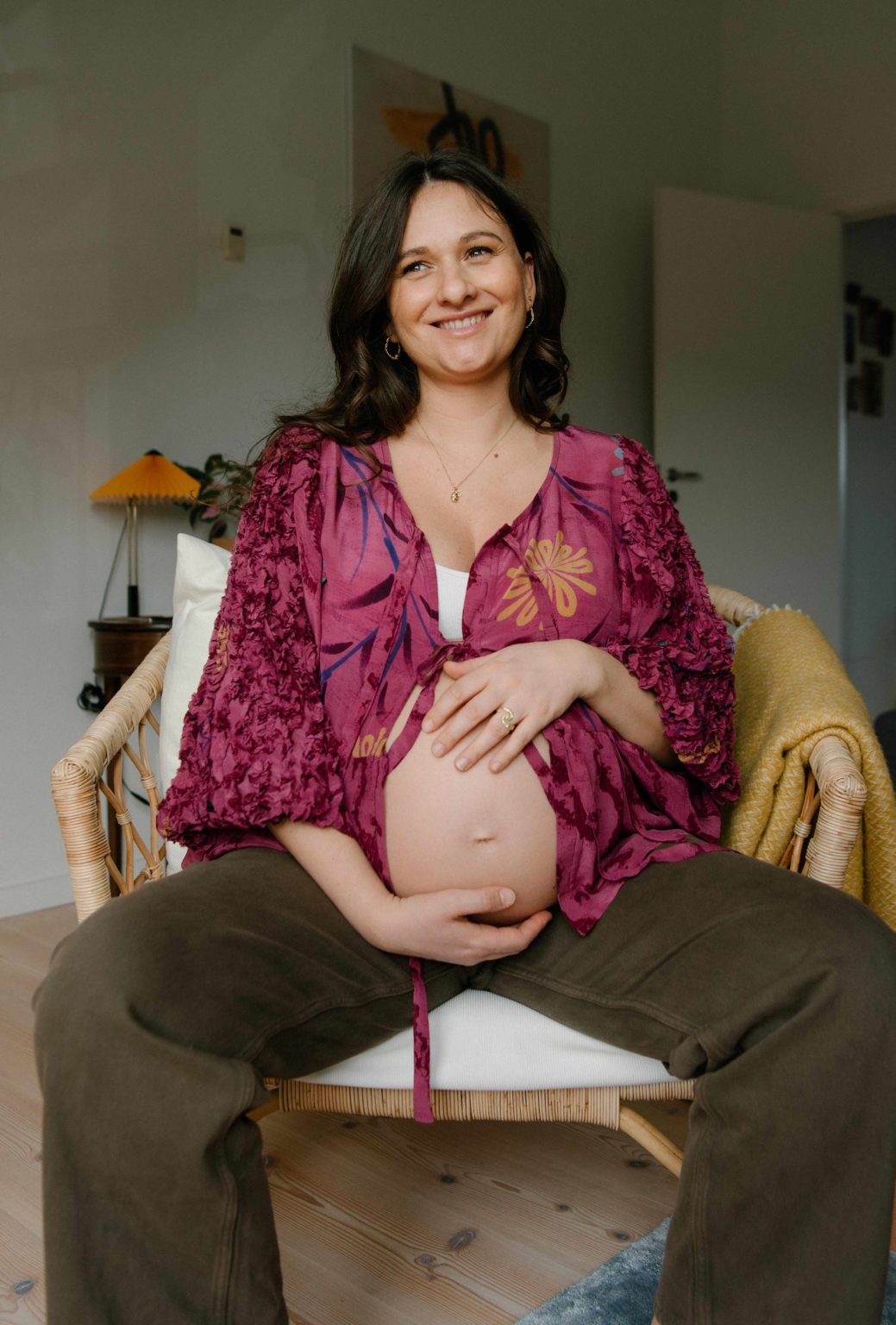 Gravid kvinde i grønne bukser lilla cardigan sidder på en stol