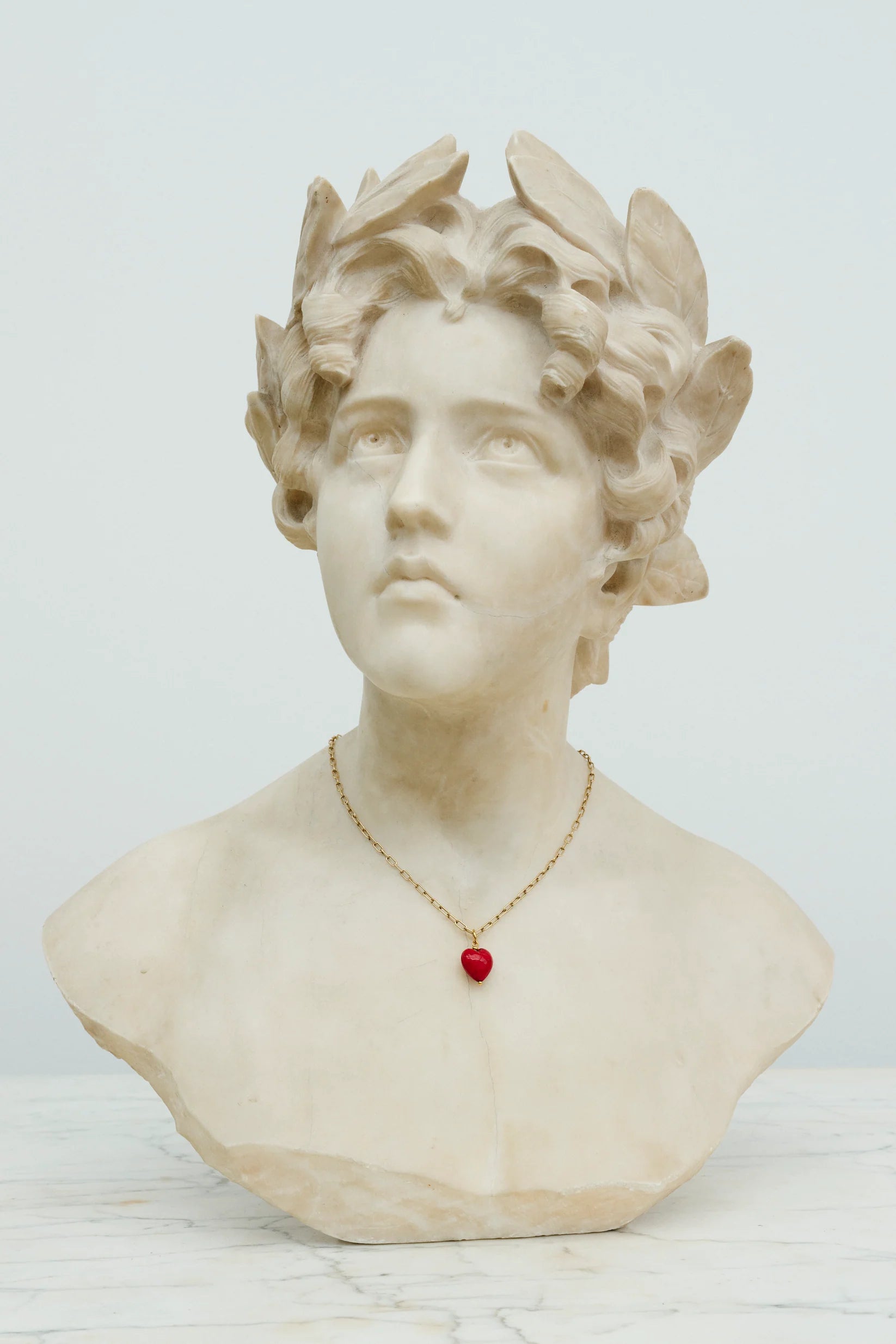 Rubinrødt hjerteformet vedhæng af muranoglas i en kæde om halsen på en statue