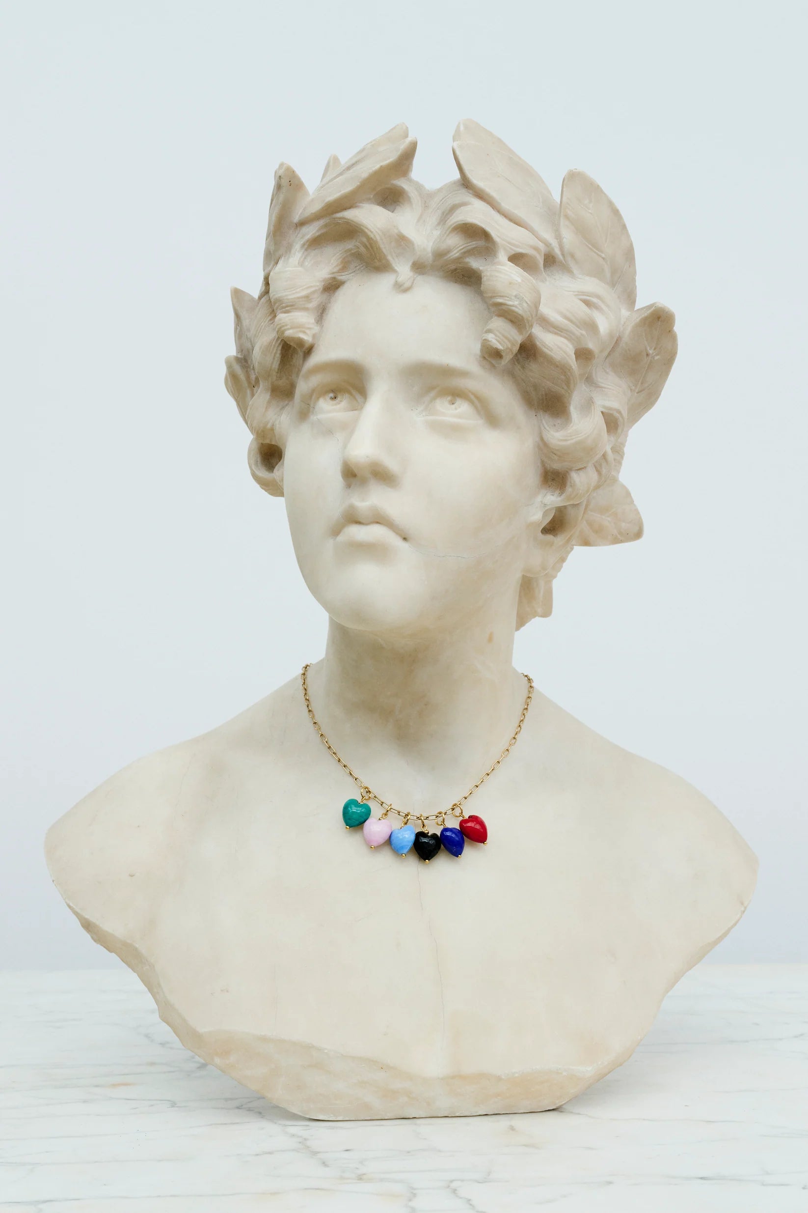 Sex hjerteformede vedhæng i forskellige farver i en kæde om halsen på en statue