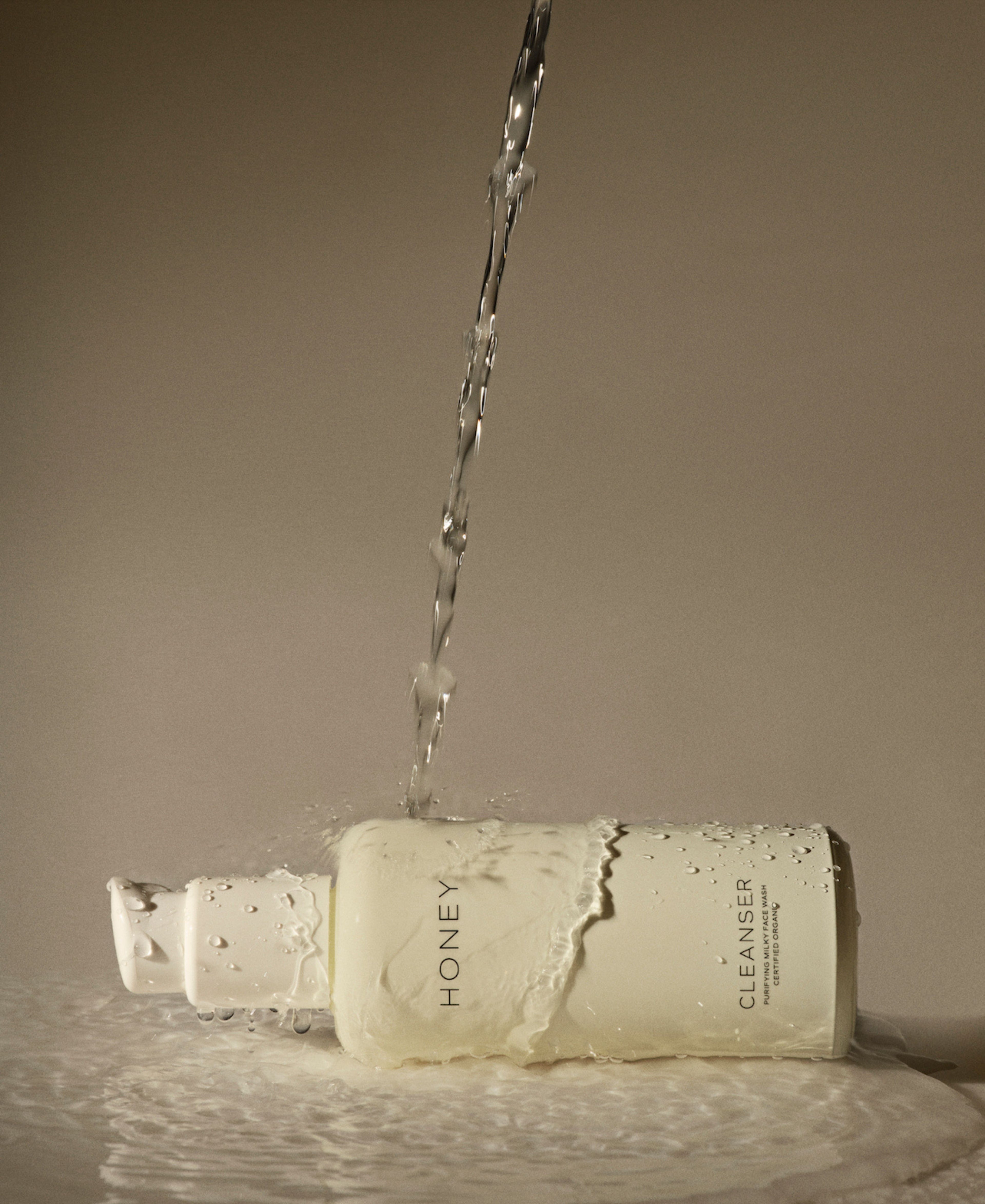 Naturlig parfumefri cleanser - ansigtsvask i lysegul flaske med hvid hætte med vand, der hældes over