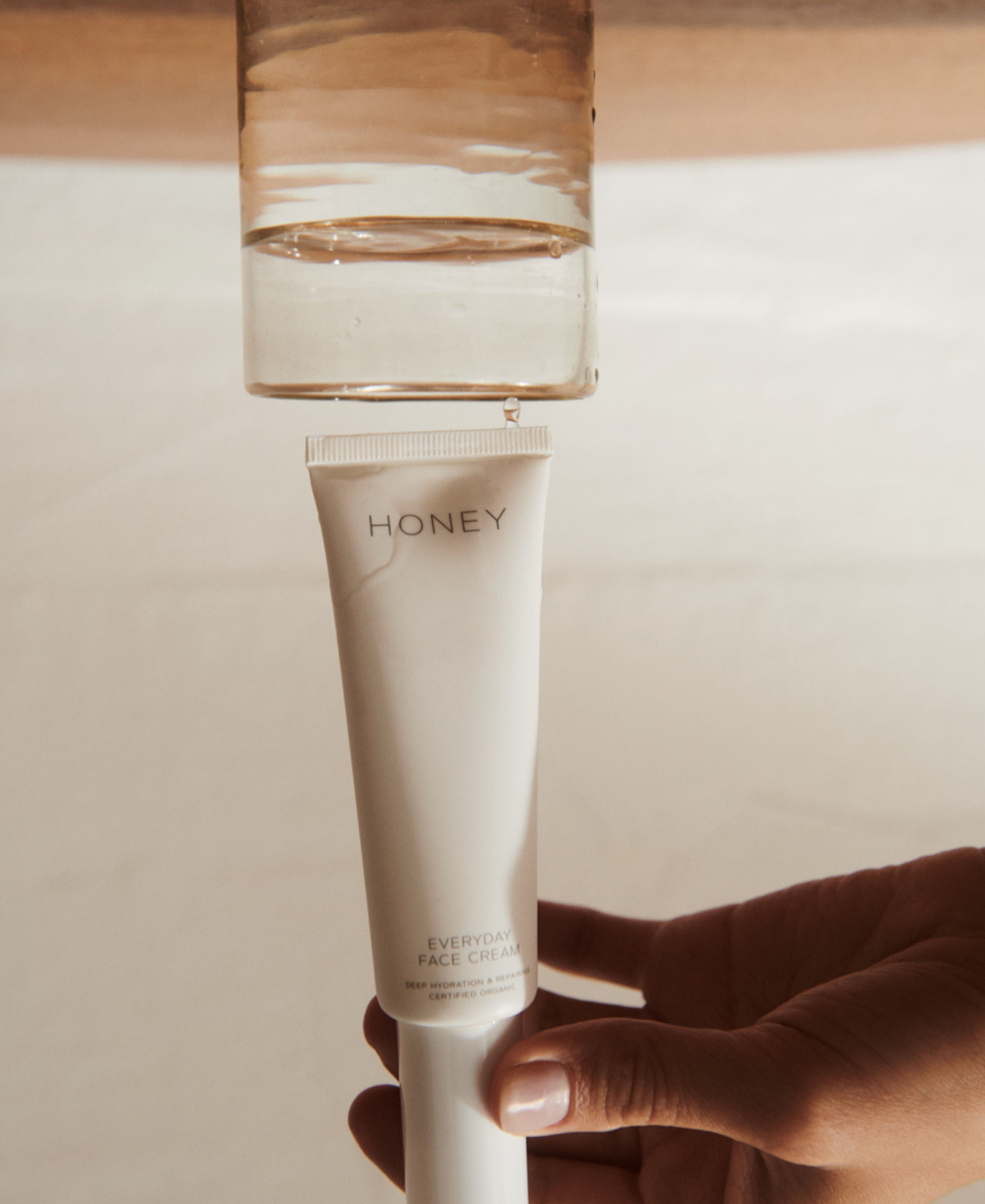 Hånd, der holder ren hudpleje ansigtscreme i lys pink tube med hvid hætte