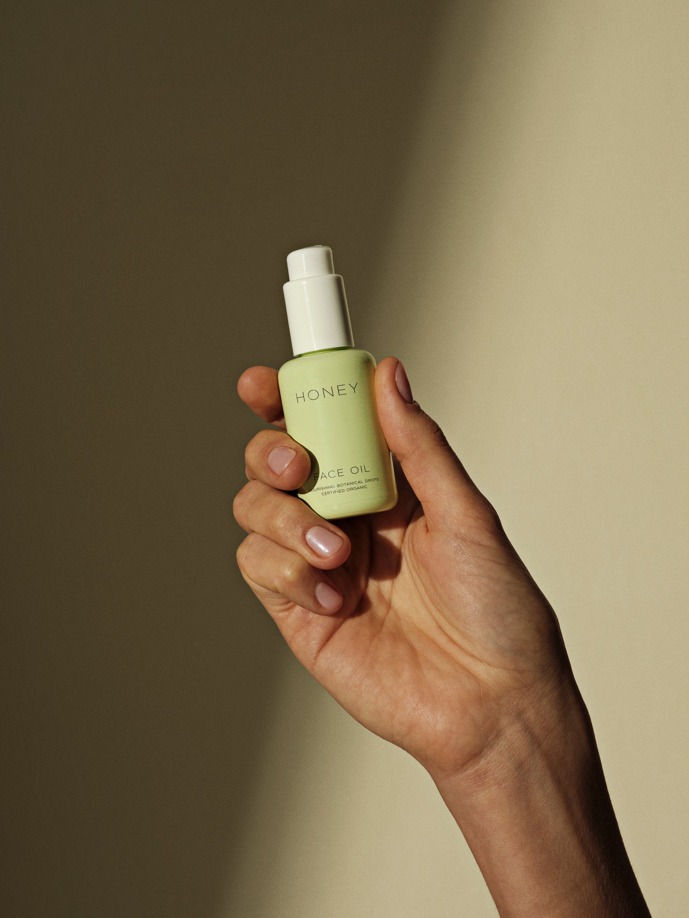 Hånd, der holder naturlig ansigtsolie i grøn flaske med hvid låg - clean skincare