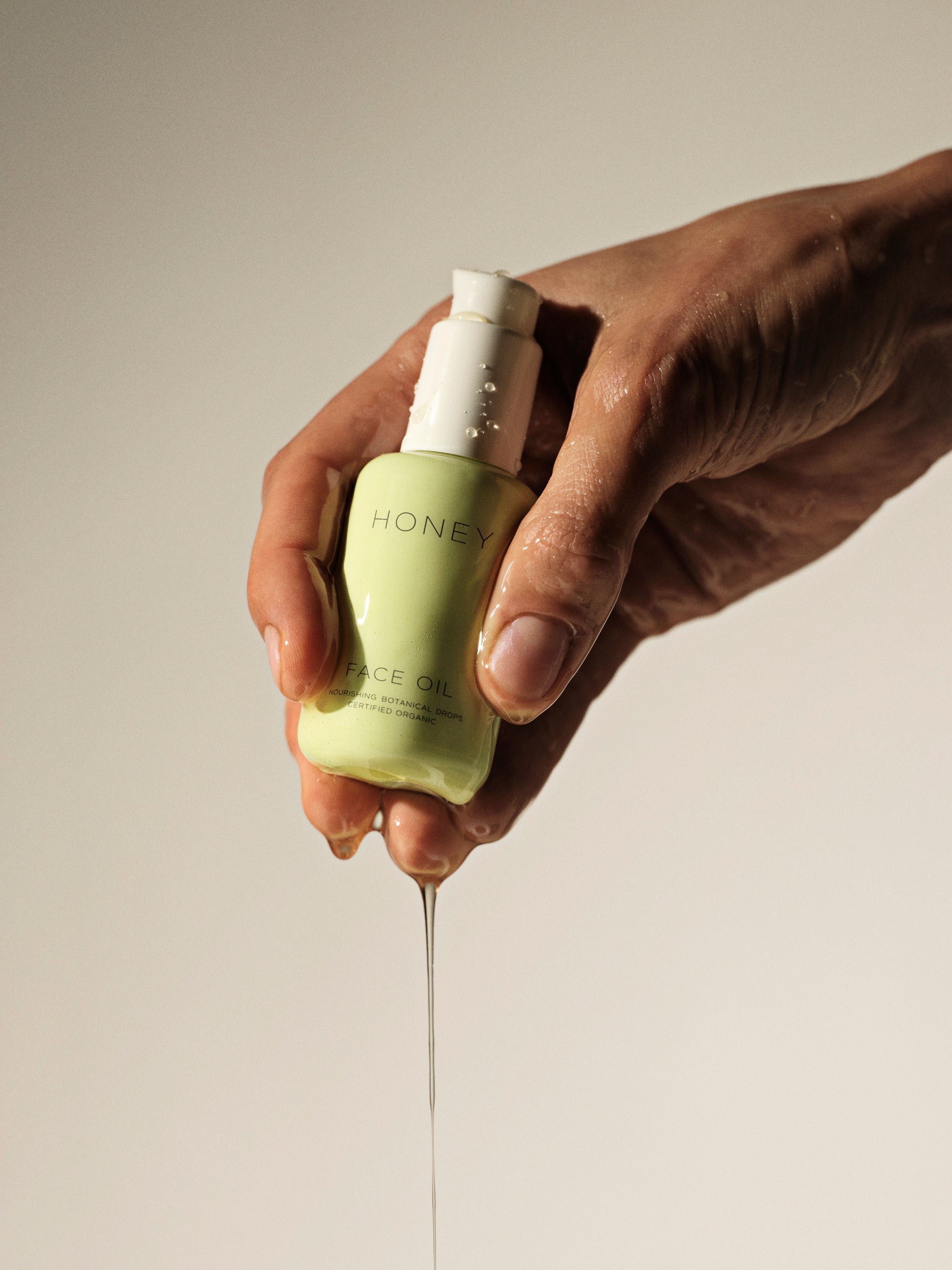 Hånd, der holder naturlig ansigtsolie i grøn flaske med hvid låg - clean skincare