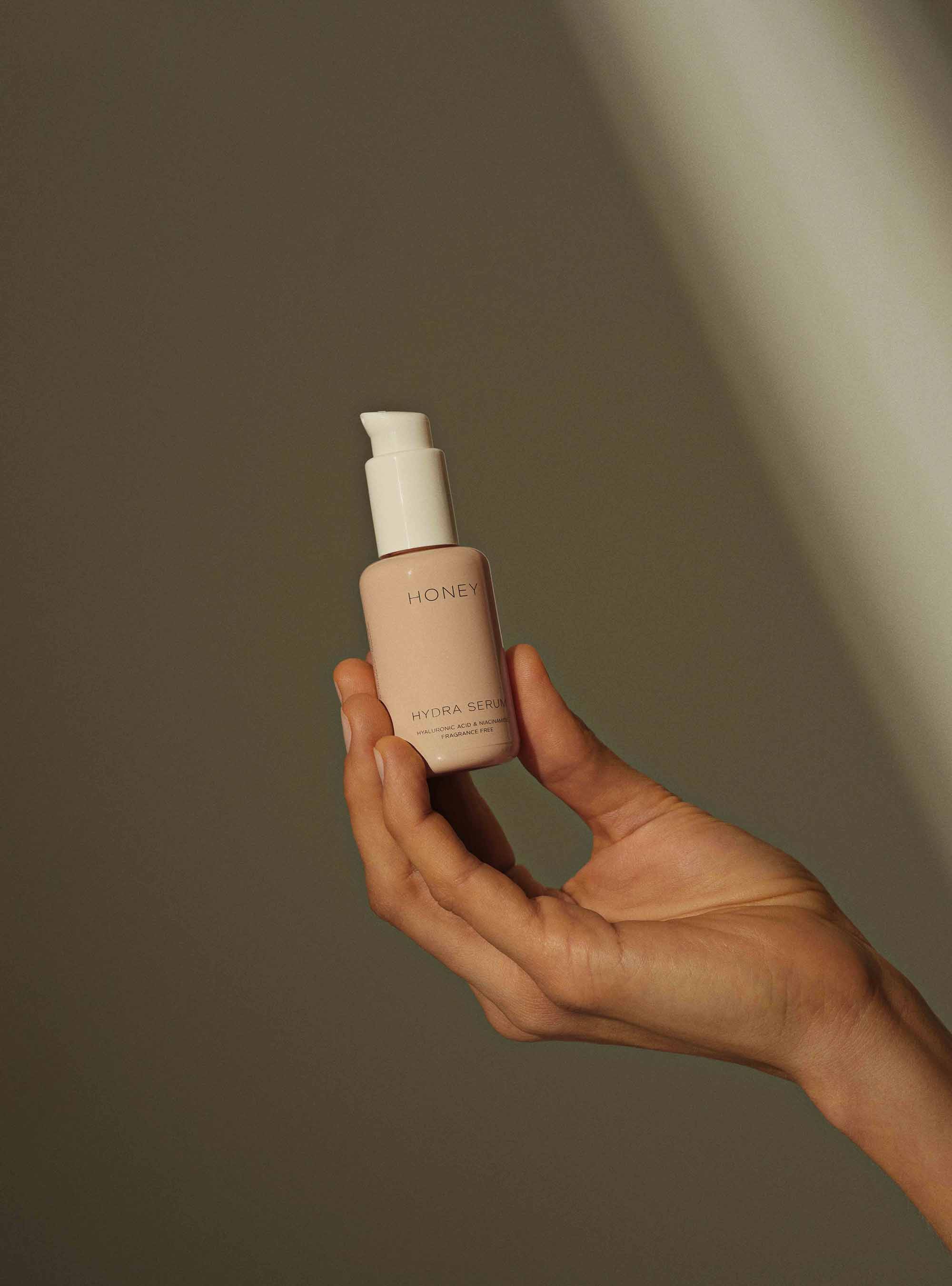 Hånd holder naturligt parfumefrit hydra-serum i støvet pink flaske med hvid låg
