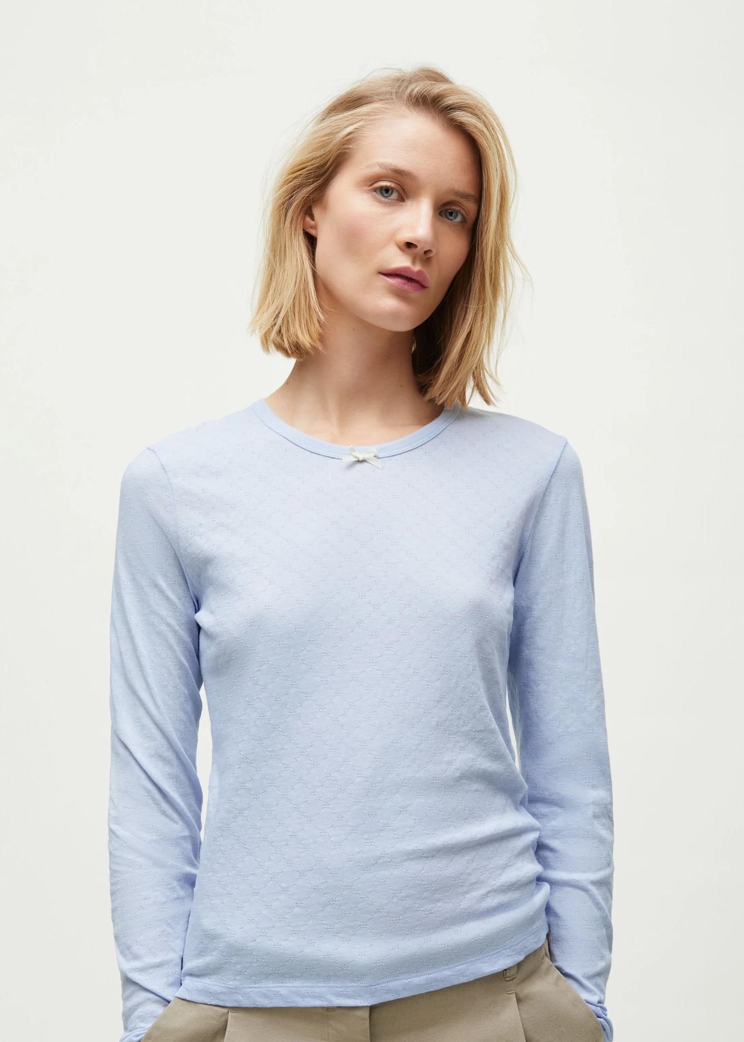 Lyshåret model med lyseblå pointelle bluse med sløjdedetalje ved halsen.
