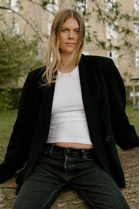 Kvinde i sorte graviditetsjeans, hvid t-shirt og sort jakke