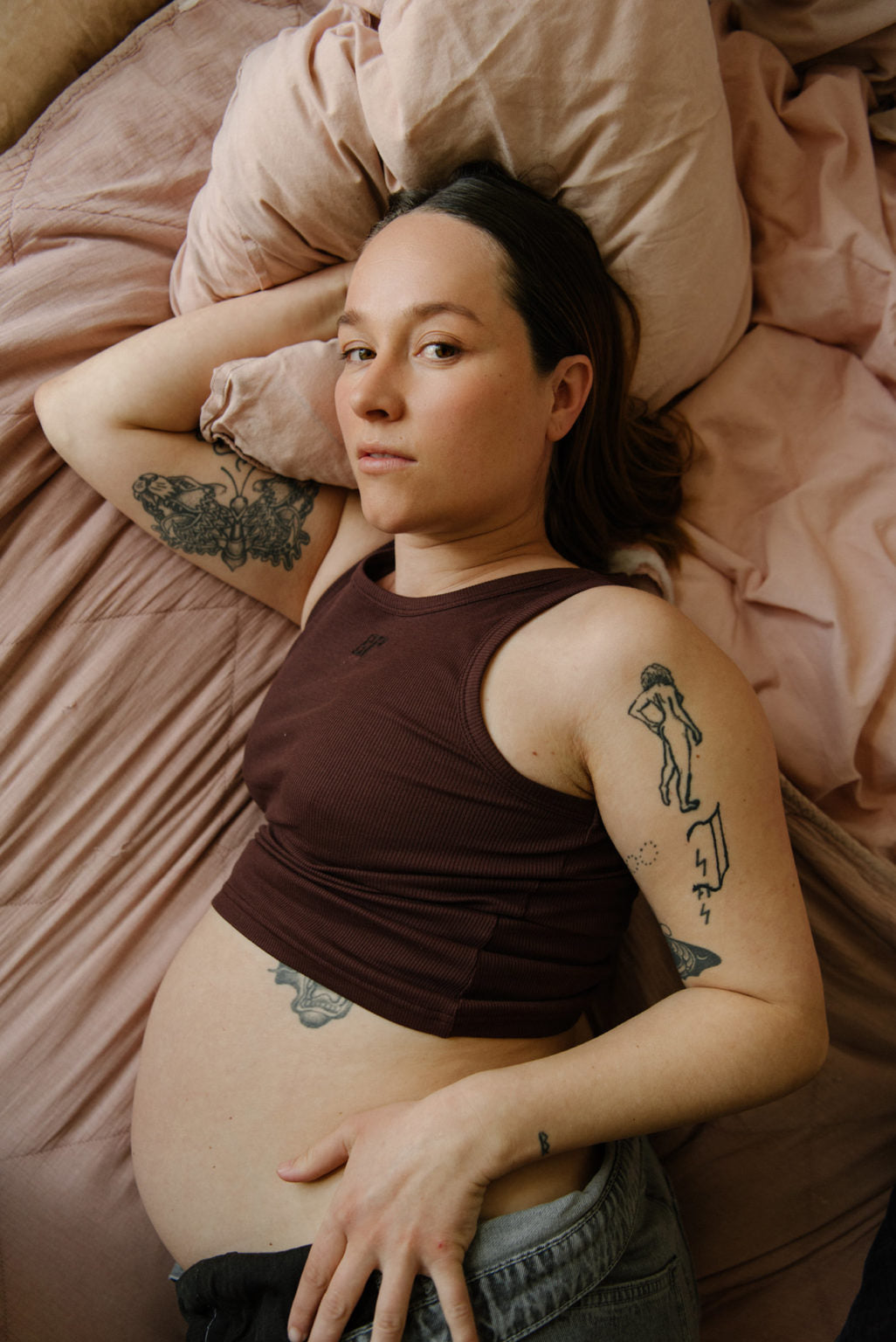 Gravid kvinde med tatoveringer liggende på sengen