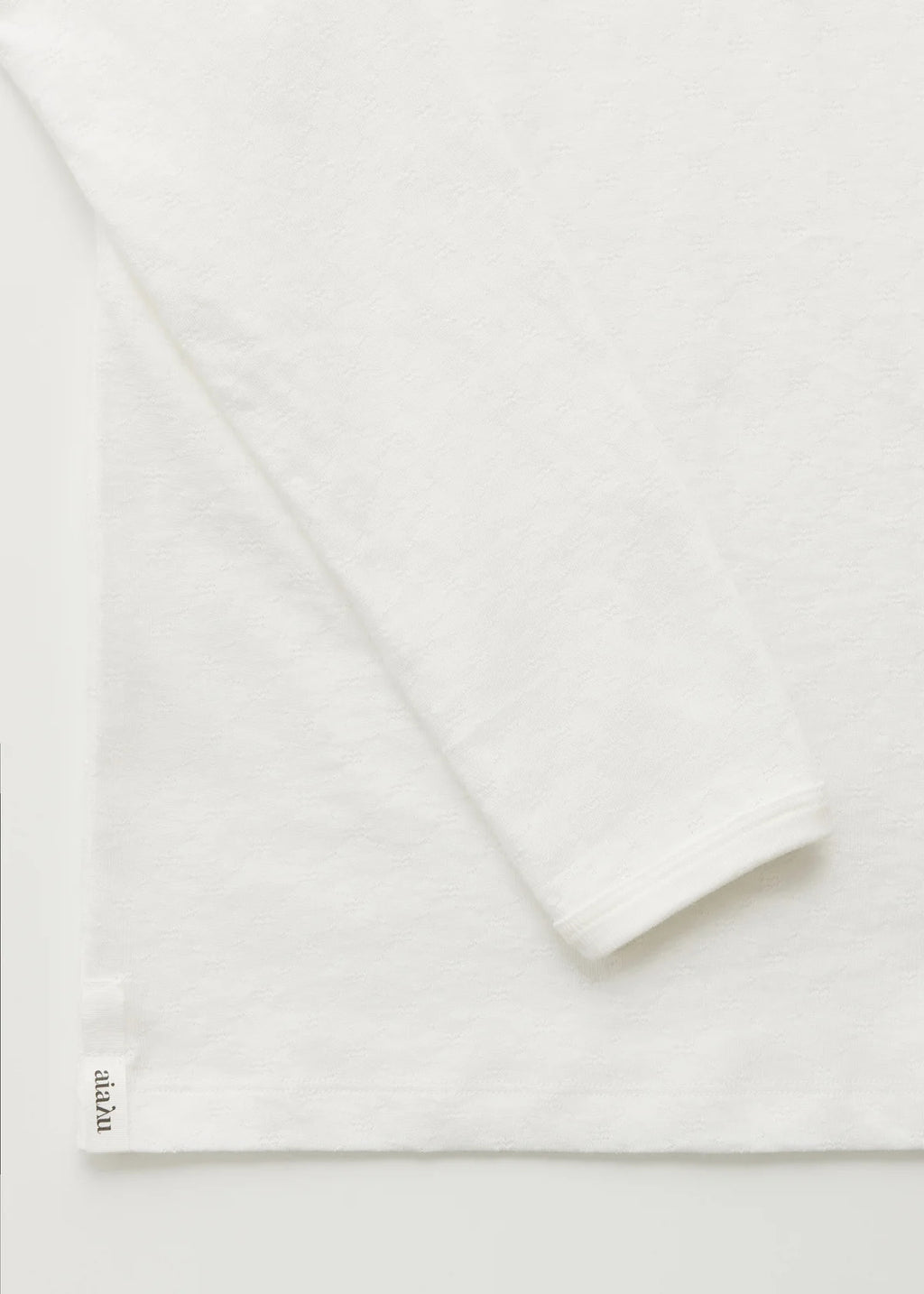 Detaljer af ærme og hjørne ad hvid bluse i pointelle.