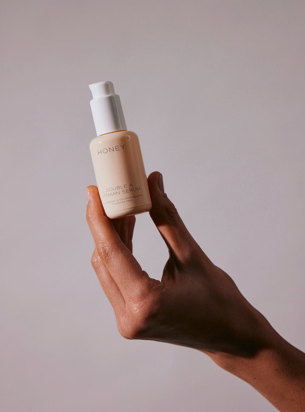 Hånd holder dobbelt A-vitaminserum i pink flaske med hvid låg - naturlig og ren hudpleje